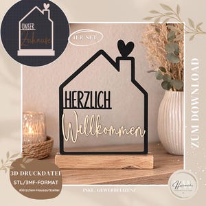 Puede incluir: Un letrero en forma de casa de madera negra y natural con las palabras "HERZLICH Willkommen" en una fuente decorativa. El letrero incluye un detalle de corazón y se asienta sobre una base de madera. La imagen también incluye el texto "3D DRUCKDATEI STL/3MF-FORMAT Klötzchen-Hausaufsteller".