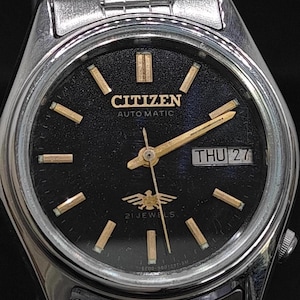 May include: A Citizen automatic wristwatch with a black face, gold-colored hands and markers, and a silver-tone stainless steel band. The watch face displays the day and date, with the day reading "THU 27". The watch has the text "CITIZEN AUTOMATIC" and "21 JEWELS".