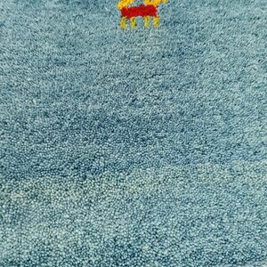 May include: Close-up of a blue rug with a small embroidered design of a horse in yellow and red. The rug has a textured surface and a green border.