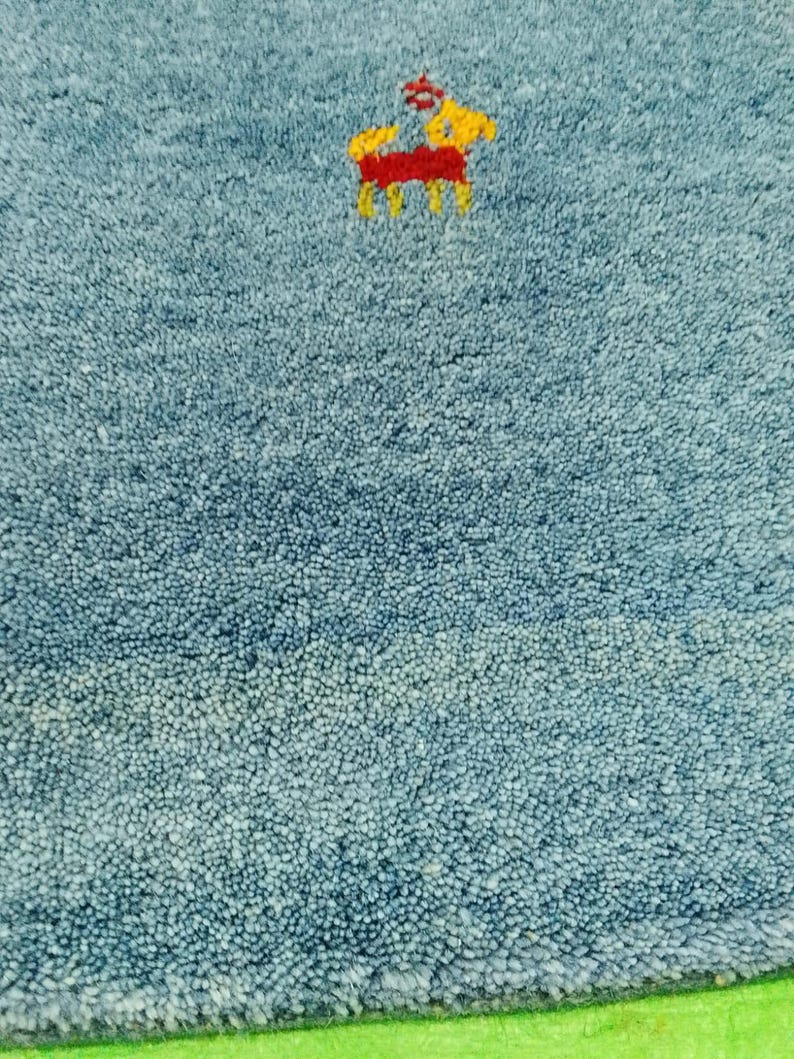 May include: Close-up of a blue rug with a small embroidered design of a horse in yellow and red. The rug has a textured surface and a green border.