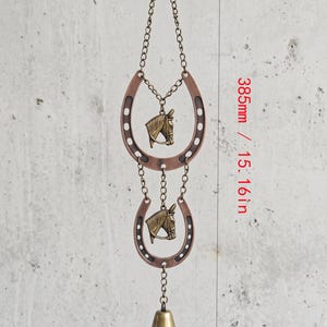 May include: A hanging ornament featuring two copper-colored horseshoes and two brass-toned horse head charms connected by metal chains, ending with a small brass bell. The total length of the item is 15.16 inches as indicated in the image.