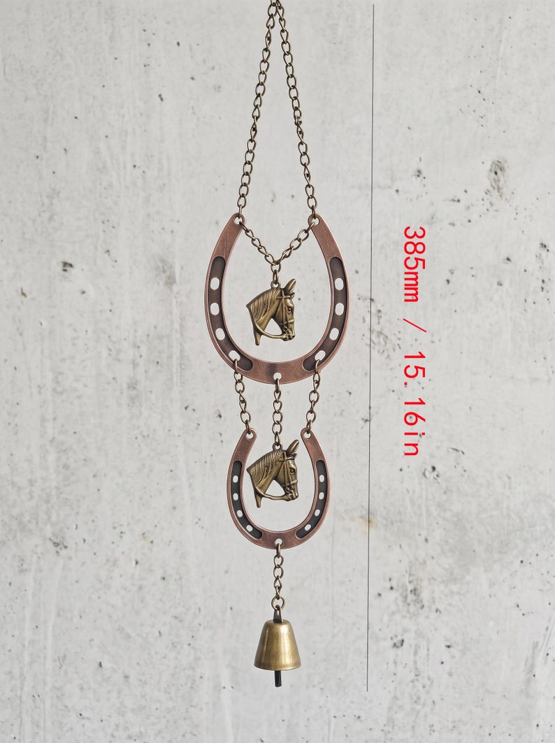 May include: A hanging ornament featuring two copper-colored horseshoes and two brass-toned horse head charms connected by metal chains, ending with a small brass bell. The total length of the item is 15.16 inches as indicated in the image.