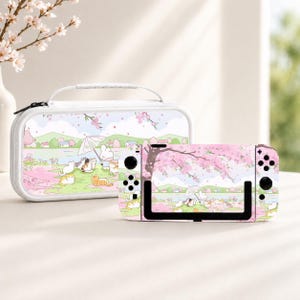 May include: A white carrying case and a handheld gaming console featuring a matching graphic print of a cartoon rabbit holding an umbrella in a park with several cats, cherry blossom trees, green hills, and a light blue sky with pink petals.