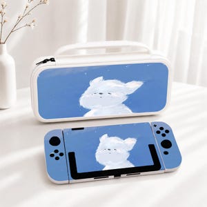 May include: A white carrying case and a handheld gaming console, both featuring a blue background with a white, fluffy, cartoon-style creature illustration. The case has a top handle and a zipper closure, while the console has black buttons.