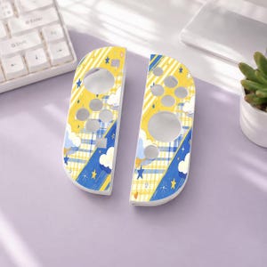 May include: Two game controller shells featuring a yellow and blue plaid pattern, white clouds, and small blue and yellow stars. The shells have circular and square cutouts for buttons and joysticks, designed for a handheld gaming console.