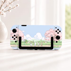 Può includere: Una skin per console di gioco portatile con cielo azzurro, alberi di ciliegio in fiore rosa e un paesaggio verde con piccoli animali dei cartoni animati che camminano lungo un sentiero. Il design include un segnale stradale con il numero 20.