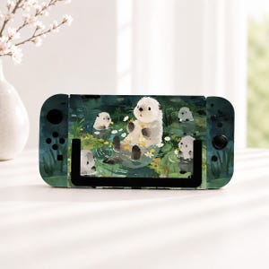 以下が含まれることがあります： 緑色の水辺をテーマにしたイラストが施された携帯型ゲーム機。白い花や黄色い花の間を泳ぐ複数のラッコが描かれています。本体の左右には黒いボタンとジョイスティックが配置されています。