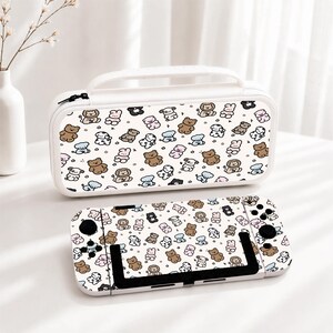 May include: A white rectangular carrying case and a handheld gaming console, both featuring a repeating pattern of small cartoon animals including brown bears, lions, and dogs on a white background. The case has a top handle and a black zipper.