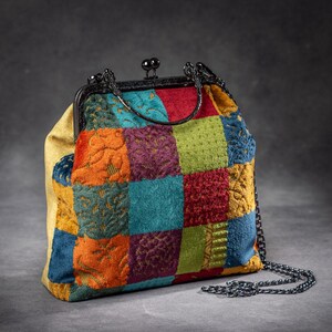 Könnte beinhalten: Eine bunte Patchwork-Handtasche mit schwarzem Metallverschluss und Kettenriemen. Die Tasche hat eine Vielzahl von strukturierten Quadraten in Rot-, Blau-, Grün-, Orange- und Lilatönen. Die Innenseite ist hellgelb.