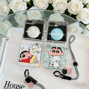 Pode incluir: Capas de telefone transparentes para Galaxy Z Flip5 com designs de personagens de desenhos animados. Cada capa apresenta uma ilustração diferente do personagem, com o texto "Crayon Shinchan" no topo. Inclui um cordão a condizer com um berloque.