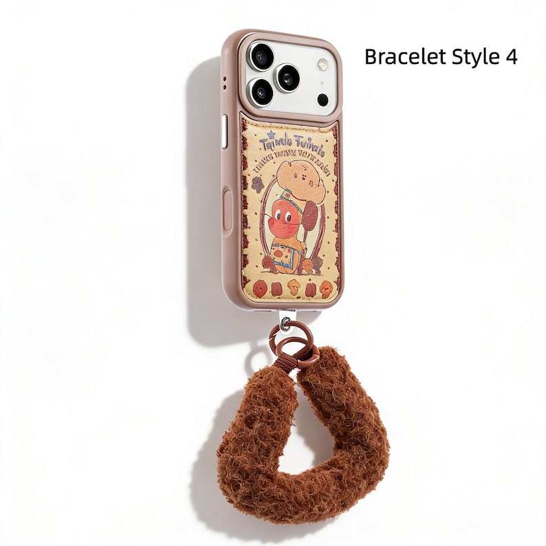 May include: A rose-gold phone case with a cartoon graphic and a brown wrist strap. The case features a whimsical illustration of a chef character. The wrist strap is made of a soft, fuzzy material.