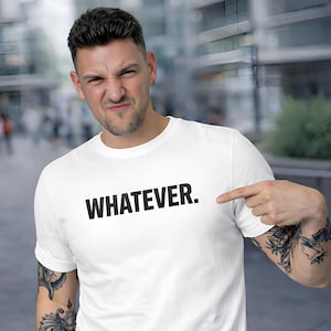 Puede incluir: Camiseta blanca con la palabra "WHATEVER." impresa en letras negras y en negrita. Una persona señala la camiseta. El fondo está borroso.