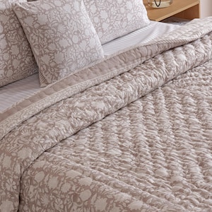 May include: A beige and white floral patterned bed set, including a comforter, pillowcases, and pillows. The bedding is arranged on a bed with a striped sheet. A vase with decorative branches sits on a wooden bedside table.