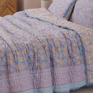 May include: A floral patterned quilt and pillow set in shades of blue, pink, and yellow. The bedding features a repeating flower design and a blue border. The quilt is on a bed with matching pillows, creating a coordinated bedroom set.