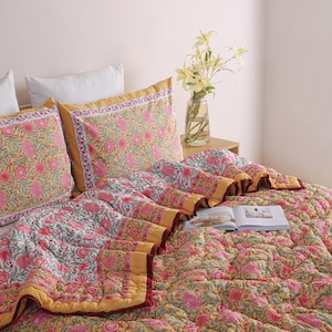 May include: A bed is made with a floral patterned quilt and two matching pillowcases. The quilt and pillowcases have a yellow background with pink and green floral designs. The quilt has a yellow border and a maroon trim.