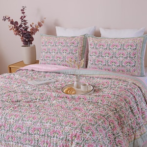 Puede incluir: Una cama está hecha con un edredón con estampado floral y fundas de almohada a juego. El edredón y las fundas de almohada tienen un fondo blanco con diseños florales rosas y verdes. Una bandeja con un cruasán y una taza de café está sobre la cama.