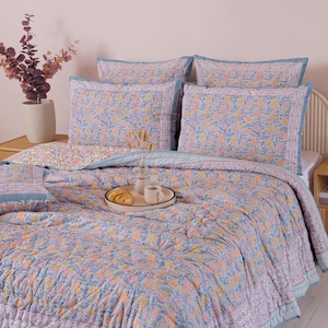 May include: A bed is made with a floral patterned quilt and matching pillowcases in shades of blue, peach, and yellow. A tray with a croissant and coffee cups sits on the quilt. The bed is in a bedroom with a neutral color palette.