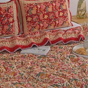 May include: A quilted bedspread and two matching rectangular pillow shams featuring a vibrant red, cream, green, and yellow floral block print pattern. The bedding set displays a detailed botanical motif with a decorative border on the pillows.