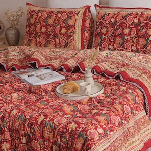 May include: A quilted bedding set featuring a vibrant red base with a repeating floral pattern in shades of yellow, pink, and green. The set includes two matching rectangular pillow shams and a large quilt, all finished with a decorative border.