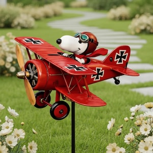 Puede incluir: Decoración de jardín de metal rojo con forma de avión, con un personaje de perro de dibujos animados que lleva un casco y gafas de piloto. El avión tiene marcas en blanco y negro y una hélice. Montado en una estaca de metal negro.