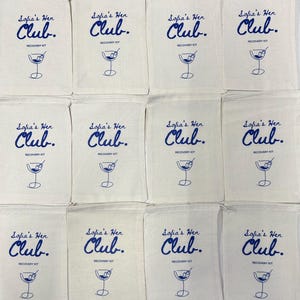 Puede incluir: Doce bolsas de algod&oacute;n de color hueso con cord&oacute;n, dispuestas en cuadr&iacute;cula. Cada bolsa tiene un estampado azul con el texto Sofia's Hen Club. RECOVERY KIT y un dibujo lineal de una copa de martini con una aceituna en un palillo.