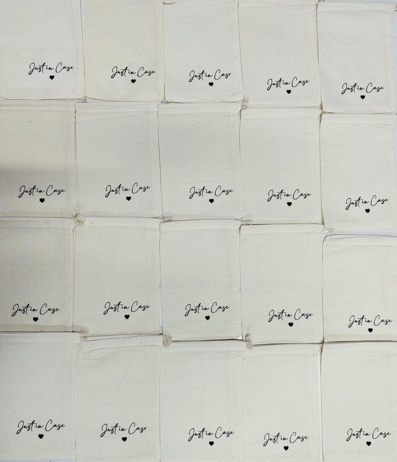 Puede incluir: Una colecci&oacute;n de veinte bolsas rectangulares de color blanco roto con cord&oacute;n, dispuestas en cuadr&iacute;cula. Cada bolsa presenta el texto impreso en negro Just in Case con un peque&ntilde;o s&iacute;mbolo de coraz&oacute;n centrado debajo de las letras.