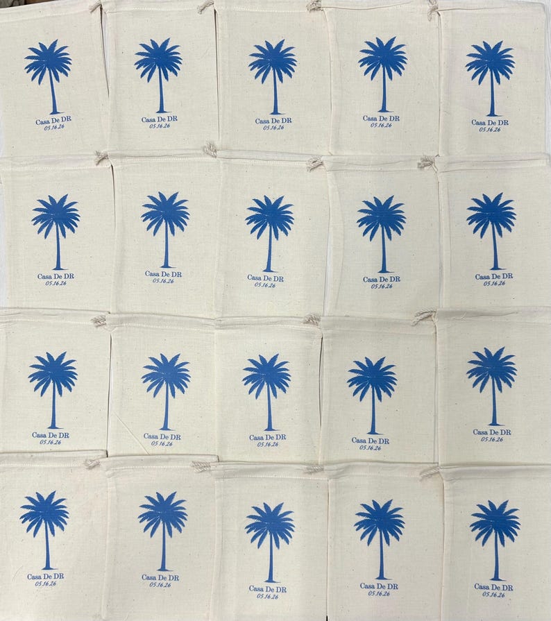 Puede incluir: Una colecci&oacute;n de veinte bolsas de tela color hueso con cord&oacute;n, dispuestas en cuadr&iacute;cula. Cada bolsa presenta un gr&aacute;fico de palmera azul impreso sobre el texto Casa De DR y la fecha 05.16.26. La tela tiene una textura tejida visible.