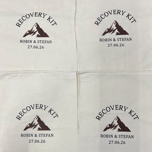 Puede incluir: Cuatro bolsas de algod&oacute;n de color blanco roto con cord&oacute;n y un dise&ntilde;o impreso en marr&oacute;n oscuro. El gr&aacute;fico incluye una ilustraci&oacute;n de monta&ntilde;a, el texto RECOVERY KIT en arco y los nombres ROBIN & STEFAN con la fecha 27.06.26 bajo la monta&ntilde;a.