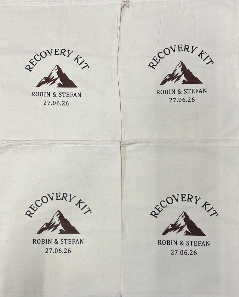 Puede incluir: Cuatro bolsas de algod&oacute;n de color blanco roto con cord&oacute;n y un dise&ntilde;o impreso en marr&oacute;n oscuro. El gr&aacute;fico incluye una ilustraci&oacute;n de monta&ntilde;a, el texto RECOVERY KIT en arco y los nombres ROBIN & STEFAN con la fecha 27.06.26 bajo la monta&ntilde;a.