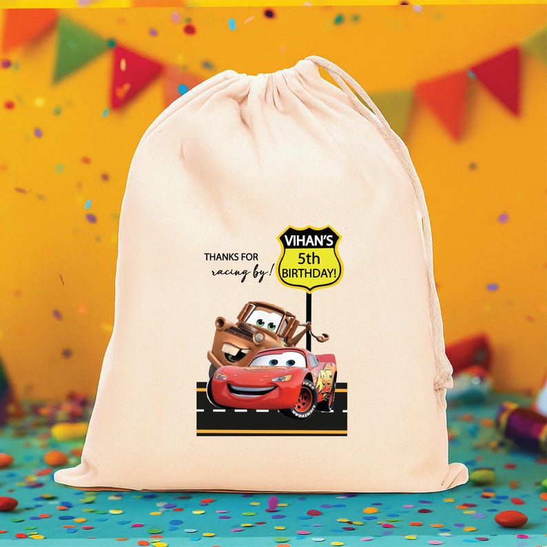Puede incluir: Una bolsa de color crema con cord&oacute;n que presenta un gr&aacute;fico de un coche de carreras rojo y una gr&uacute;a marr&oacute;n sobre una carretera negra. Sobre los veh&iacute;culos hay una se&ntilde;al amarilla con el texto VIHAN'S 5th BIRTHDAY! y THANKS FOR racing by!