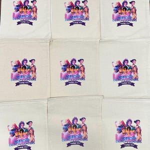 Puede incluir: Un conjunto de nueve bolsas de algod&oacute;n de color blanco roto con cord&oacute;n, cada una con un gr&aacute;fico impreso de un grupo de personajes estilo anime. Debajo de los personajes, el texto KPOP DEMON HUNTERS y THANK YOU aparece en una banda morada.