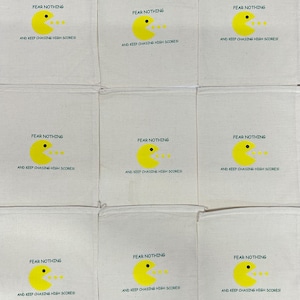 Puede incluir: Nueve bolsas de algod&oacute;n de color blanco roto con cord&oacute;n dispuestas en una cuadr&iacute;cula. Cada bolsa presenta un gr&aacute;fico de personaje circular amarillo con un ojo negro y la boca abierta, junto al texto FEAR NOTHING AND KEEP CHASING HIGH SCORES en negro.