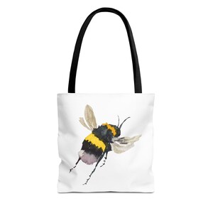 Può includere: Borsa tote bianca con un'illustrazione ad acquerello di un calabrone in volo. L'ape ha strisce gialle e nere, con ali traslucide. La borsa ha manici neri.