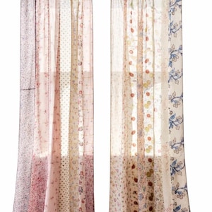 May include: Two sheer, patchwork-style curtains. The curtains feature a variety of floral and patterned fabrics in shades of pink, cream, and blue. They are hung on a black rod with fabric loops.