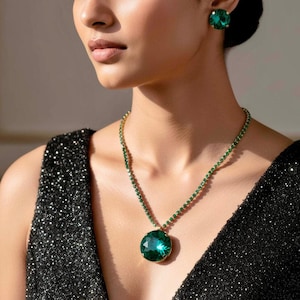 May include: A jewellery set consisting of a necklace and a stud earring featuring round, faceted emerald green crystals set in gold-toned metal. The necklace has a delicate chain of small green stones leading to a large, circular pendant.