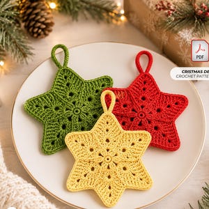 Op de afbeelding: Drie stervormige gehaakte ornamenten in groen, rood en geel, elk met een centraal cirkelvormig motief en een kleine ophanglus. De tekst CRISTMAS DECOR CROCHET PATTERN PDF is zichtbaar in de rechterbovenhoek van de afbeelding.
