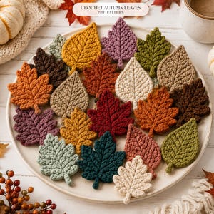 May include: A collection of crocheted autumn leaves in various shapes and colors including mustard, dark red, forest green, cream, brown, and sage, arranged on a round plate with a label reading CROCHET AUTUMN LEAVES PDF PATTERN.