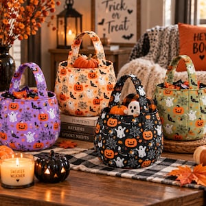 May include: Four fabric Halloween trick-or-treat baskets with handles, featuring patterns of orange pumpkins, white ghosts, and black spiderwebs. The baskets come in purple, orange, black, and green colors, each filled with assorted candy treats.