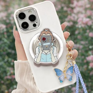 May include: White phone case with a clear ring holder featuring a cartoon image of a woman holding a book with the word "BOOKISH". A blue and silver butterfly charm hangs from the case.