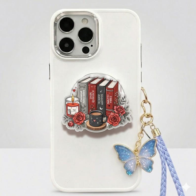 May include: A white smartphone case featuring a sticker of four books labeled Twisted Fairy Tales, Dark Romance, Trigger Warnings, and Smutty Vibes, alongside a lit candle, a mug, and red roses, with a blue butterfly charm on a braided strap.