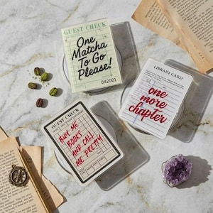 Op de afbeelding: Drie doorzichtige acryl onderzetters met de tekst: "One Matcha To Go Please!", "Buy Me Books And Call Me Pretty" en "one more chapter". De onderzetters liggen op een marmeren oppervlak met koffiebonen en een paars kristal.