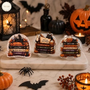 May include: Three clear acrylic ornaments featuring stacks of books with Halloween themes. The designs include text such as Just a Girl Who Loves Spooky Nights and Halloween, Just One More Chapter, and Pumpkin Spice, Magic and Spells, and Cozy Nights.