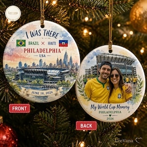May include: Two round ceramic ornaments featuring a watercolor illustration of the Philadelphia skyline and Lincoln Financial Field on the front with the text I WAS THERE BRAZIL X HAITI PHILADELPHIA USA JUNE 18, 2026 and a photo on the back.