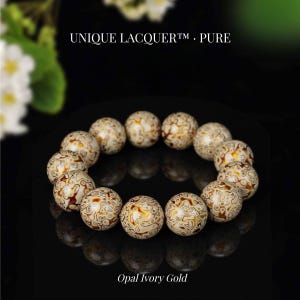Puede incluir: Un brazalete de cuentas redondas en tonos marfil, dorado y marrón. Las cuentas tienen un diseño único. El texto "UNIQUE LACQUER. PURE" está en la parte superior y "Opal Ivory Gold" en la inferior.
