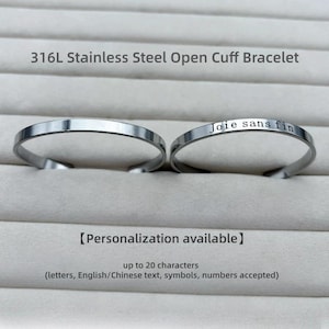 May include: Two silver-coloured 316L stainless steel open cuff bracelets. One bracelet is plain, and the other is engraved with the text 'Joie sans fin'. The image includes the text '316L Stainless Steel Open Cuff Bracelet' and 'Personalization available' with details about character limits.