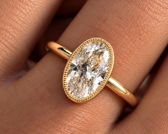 Peut inclure: Une bague en or avec une pierre précieuse transparente de taille ovale, sertie dans un chaton à bordure perlée. L'anneau est lisse et poli, mettant en valeur le design classique de la pierre facettée et la teinte chaude du métal.