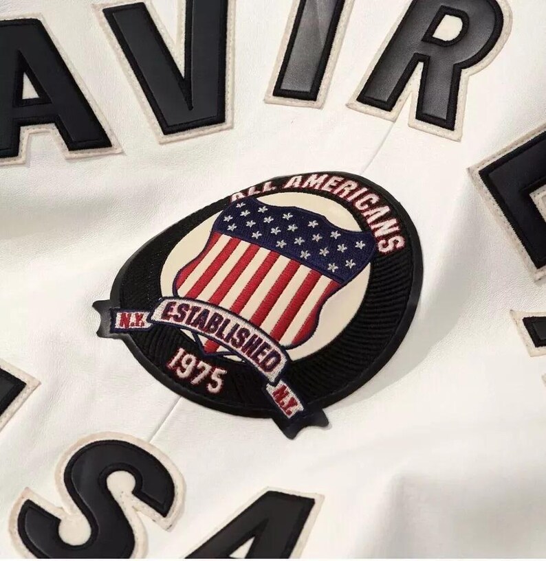 May include: White jacket with black lettering and a patch featuring the American flag. The patch reads "ALL AMERICANS ESTABLISHED 1975 N.Y." The jacket has a classic, sporty aesthetic.