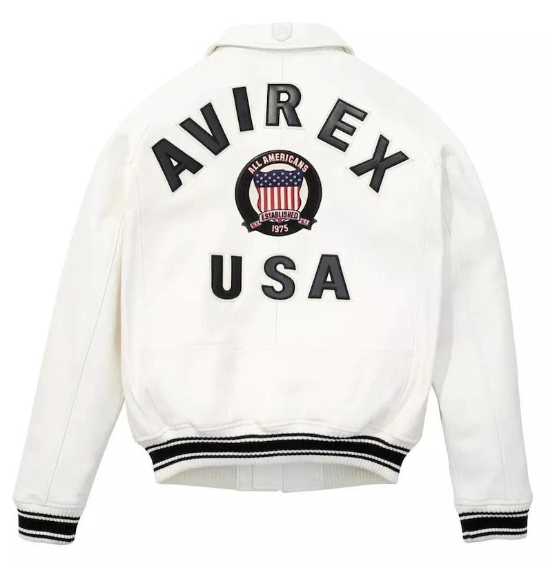 May include: White jacket with black and white striped trim on the cuffs and hem. The back features the text "AVIREX USA" in black, with a circular emblem that includes the words "ALL AMERICANS ESTABLISHED 1975".