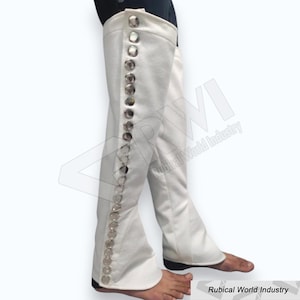 May include: White, knee-high boots with a row of large, silver-colored buttons down the side. The boots have a slight flare at the bottom and are made of a smooth, possibly satin-like material. The boots are shown on a person's legs.