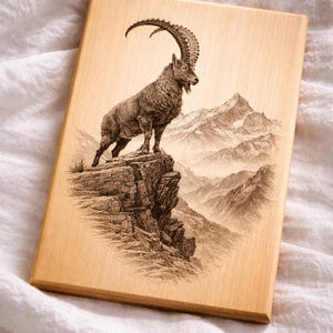 Może przedstawiać: Drewniana tablica z szczegółowym grawerunkiem koziorożca na klifie, z górami w tle. Grafika jest w odcieniach brązu i beżu, tworząc rustykalną estetykę.